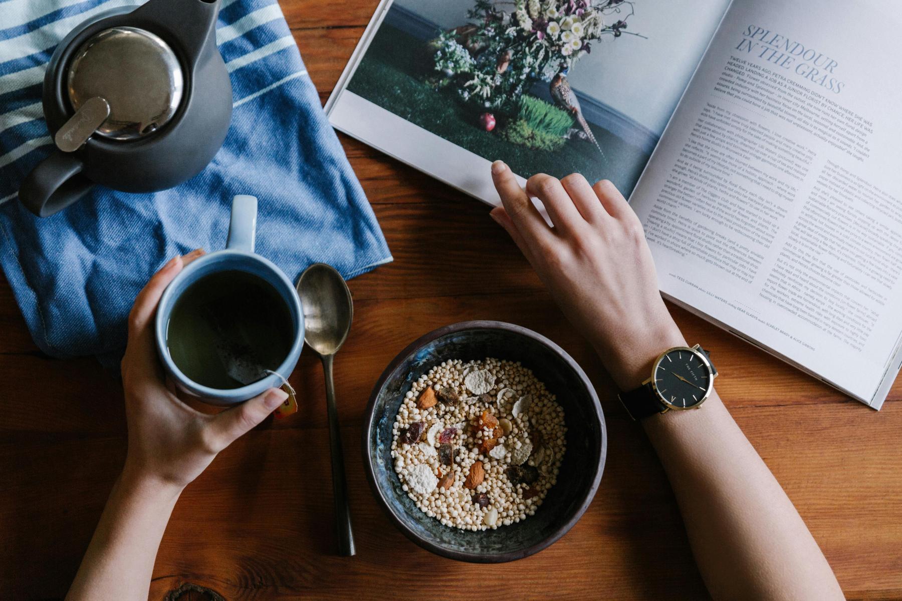 person drinking coffee and eating healthy breakfast while browsing a book